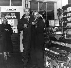 General stores were welcome places to gather and chat or play cards. At the Waldemar store, Jack Lomas and Billy Miller are about to offer a bit of music in front of the Star Weekly bench as Doris Miller looks on. Photo Courtesy Waldemar Tweedsmuir History.
