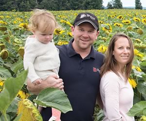 Sean and Amy Davis with baby Nora amid sunflowers they grow for birdseed at Davis Feed & Farm Supply. Photo by Pete Paterson.