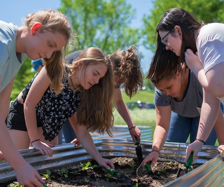 A sunny spring day gets students Sarah Baker, Megan Crane, Maggie Claus, Mikayla Clarke and Amanda Cote outside to plant fast-growing crops such as red leaf lettuce, spinach and kale. Photo by James MacDonald.