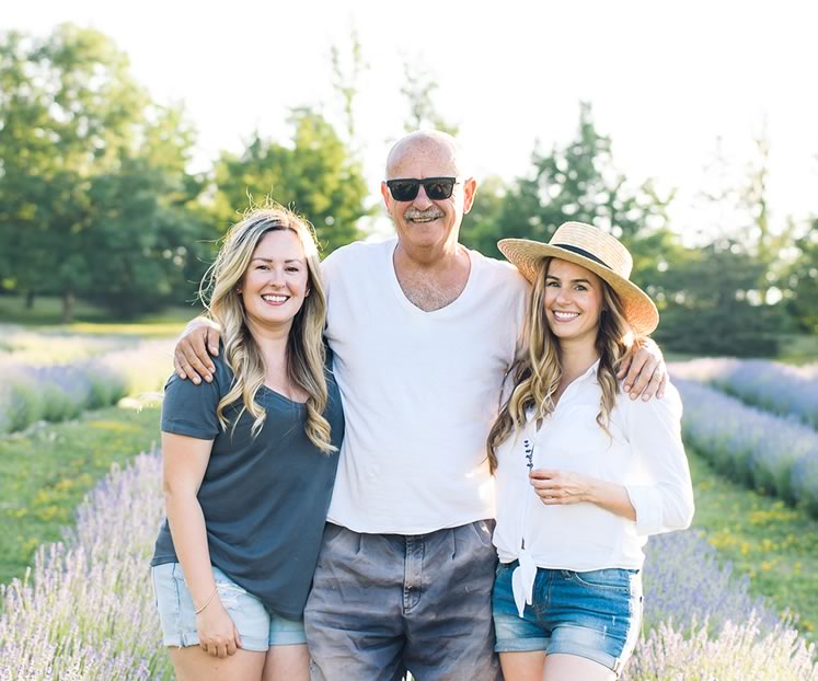 At their family farm near Creemore, Emma Greasley, left, and Jessica Ridding flank their father, Brian Greasley, between rows of lavender. Photo by Jessica Crandlemire, Light and Shadow Photography.