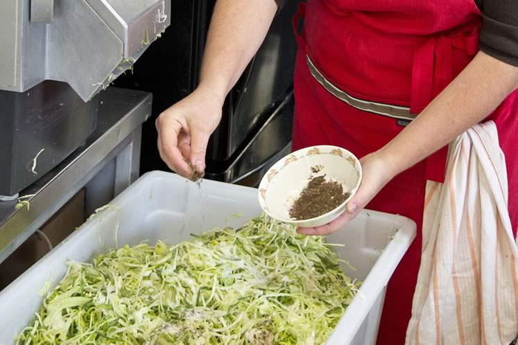 Andrea adds sliced leeks, wild greens, garlic, salt and pepper to a sauerkraut blend. Photo by Pete Paterson.