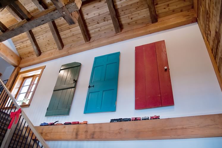 A trio of brightly painted wooden doors, salvaged from the original log cabin on the property, hang as art above the staircase to the second floor. Photo by Rosemary Hasner / Black Dog Creative Arts.